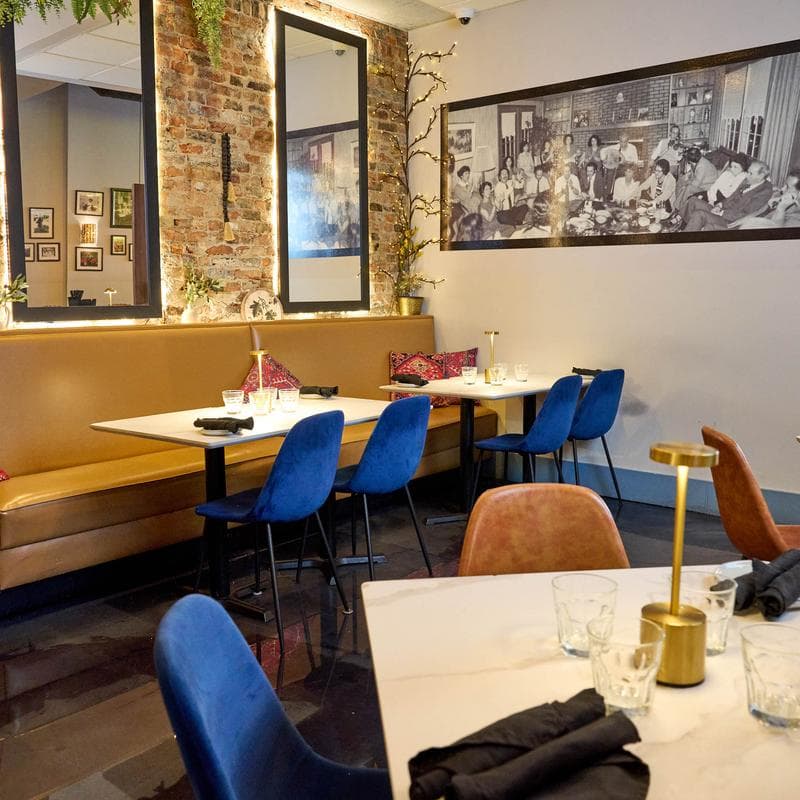 Dining area with set marble tables, blue chairs, framed art, and festive decor