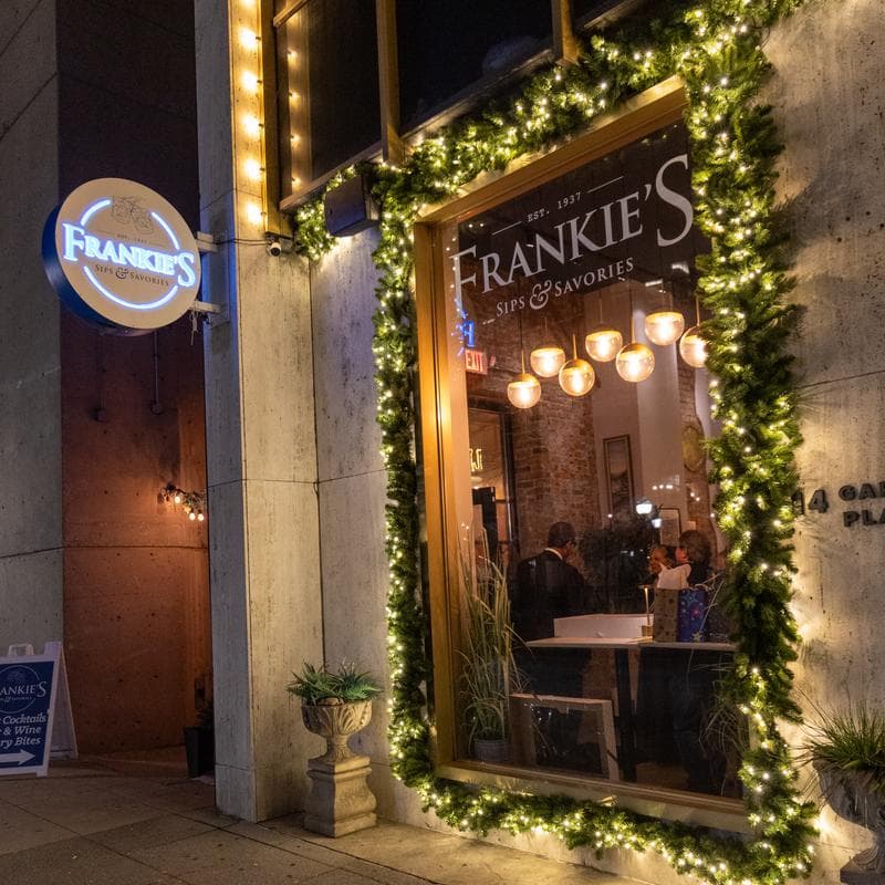 Frankie's Sips and Savories storefront with signage and lit Christmas garland decor