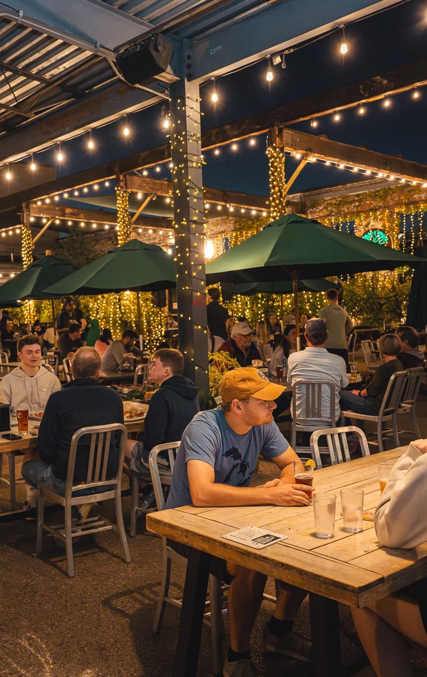 Crowded beer garden with string lights and green umbrellas at MadTree Oakley taproom