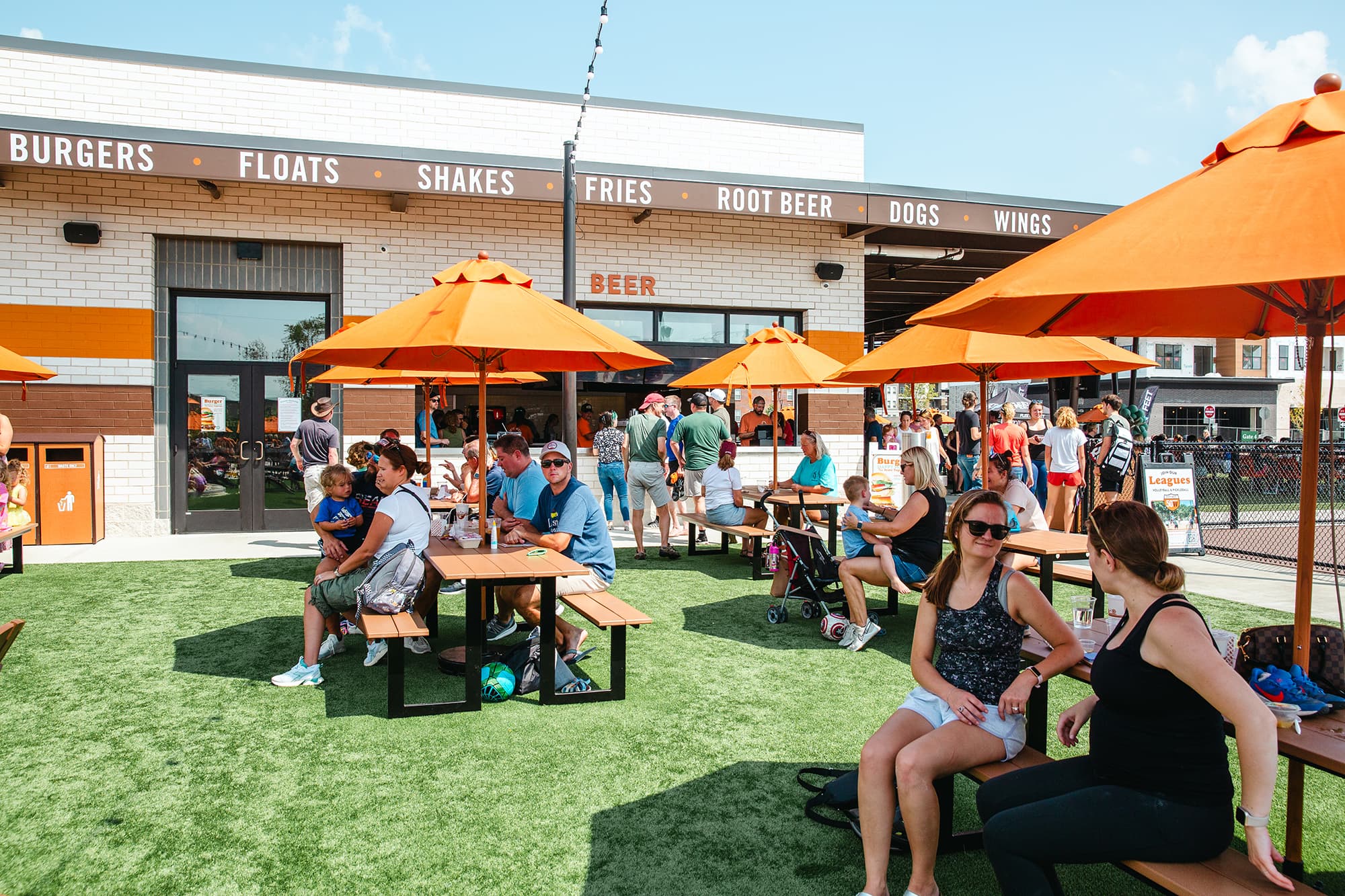 Guests seated under orange umbrellas outside the Fifty West Deerfield burger bar and patio.
