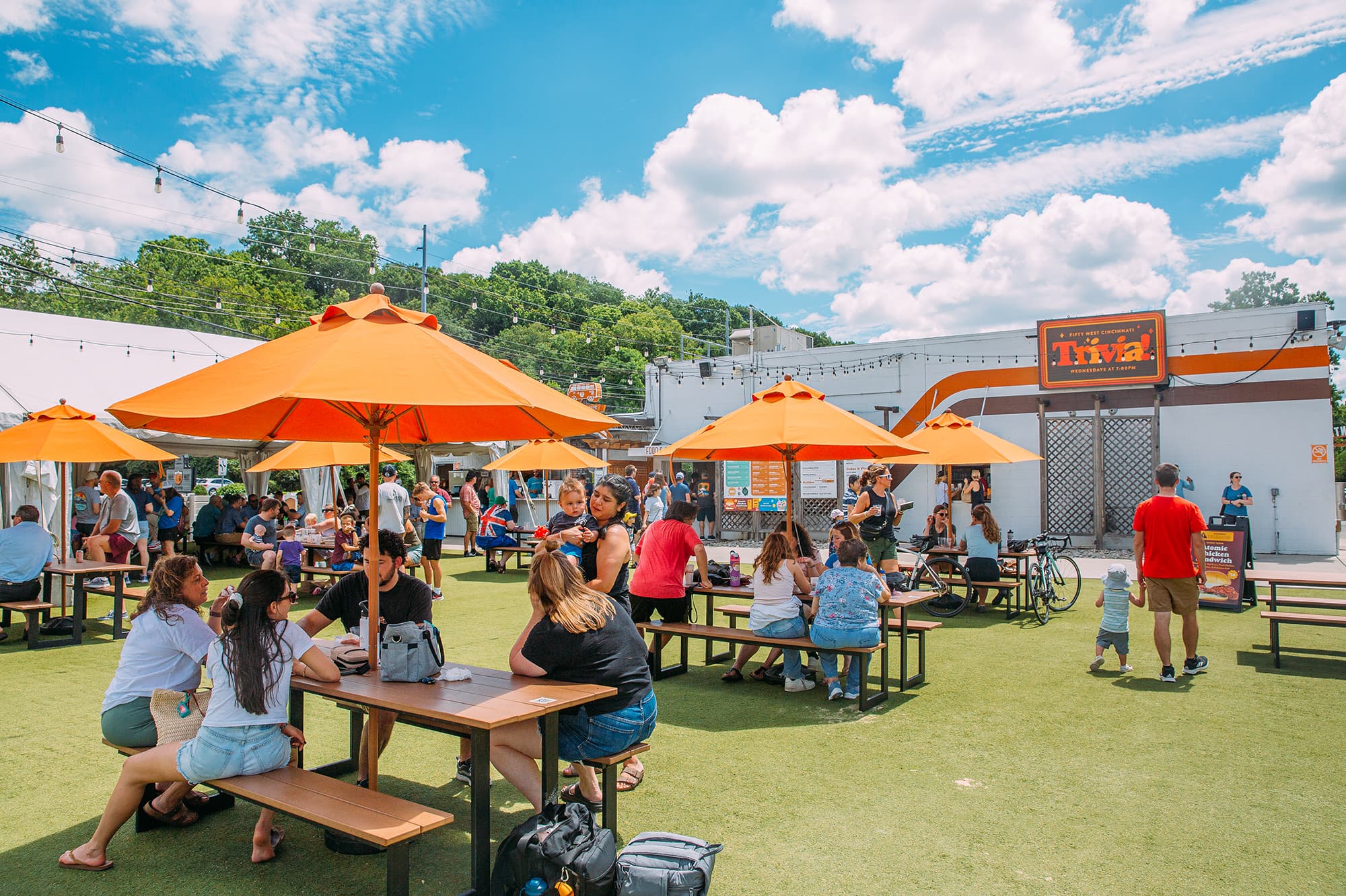 Families seated at orange umbrella picnic tables on the 50 West Brewing Wooster Pike patio.