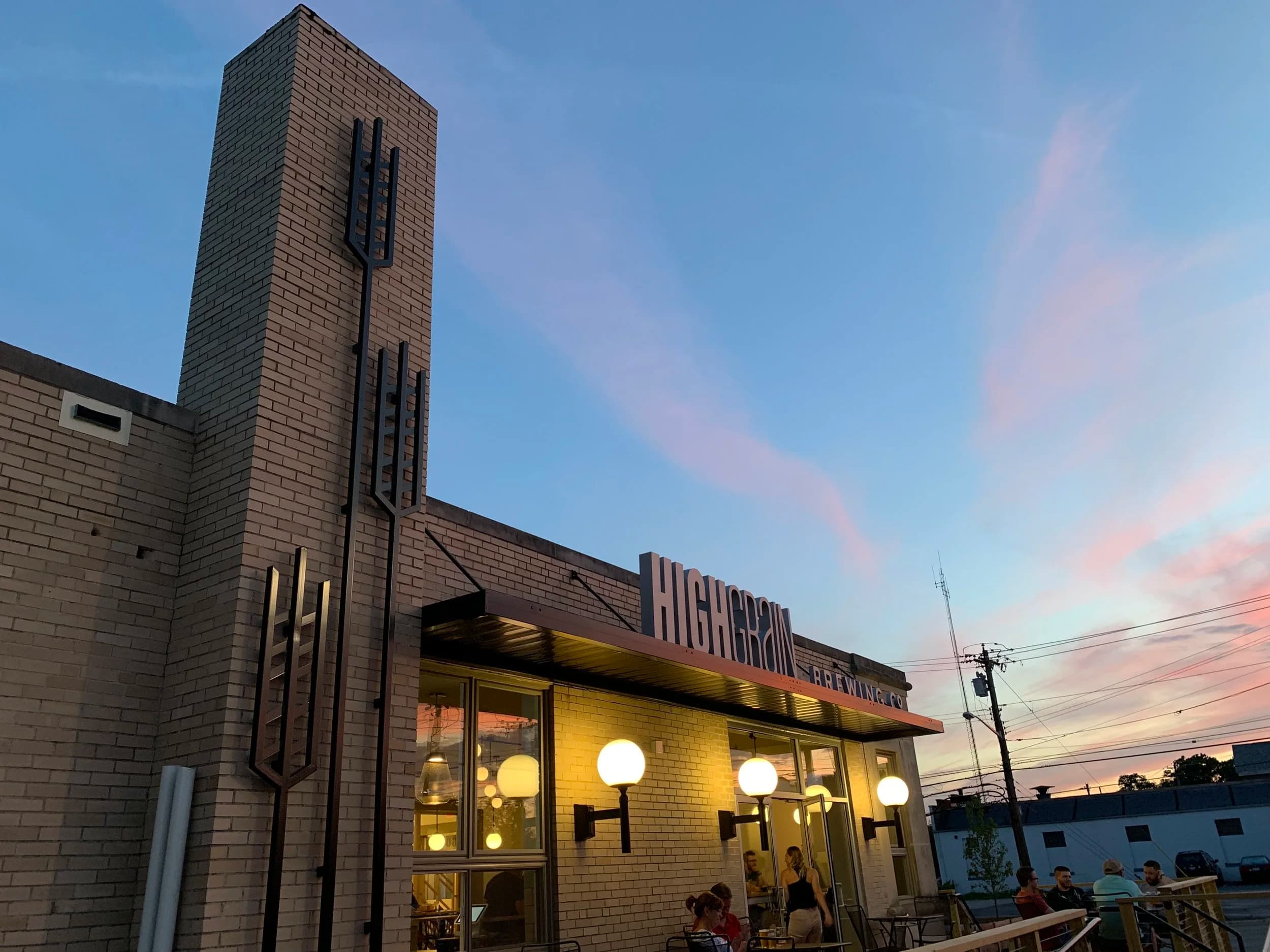 Exterior of High Grain Brewing at dusk with outdoor seating and decorative lighting
